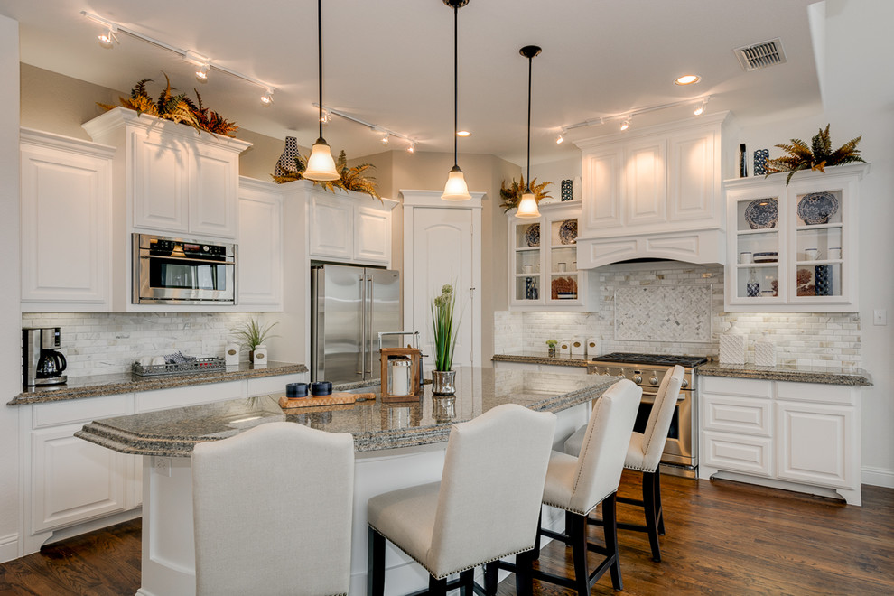 Photo of a traditional l-shaped open plan kitchen in Dallas with a double-bowl sink, raised-panel cabinets, white cabinets, granite benchtops, beige splashback, porcelain splashback, stainless steel appliances, dark hardwood floors and with island.