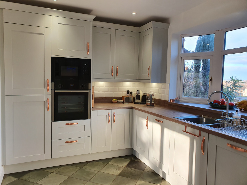 Mid-sized contemporary u-shaped separate kitchen in West Midlands with a double-bowl sink, shaker cabinets, grey cabinets, laminate benchtops, metallic splashback, glass sheet splashback, black appliances, ceramic floors, no island, multi-coloured floor and brown benchtop.