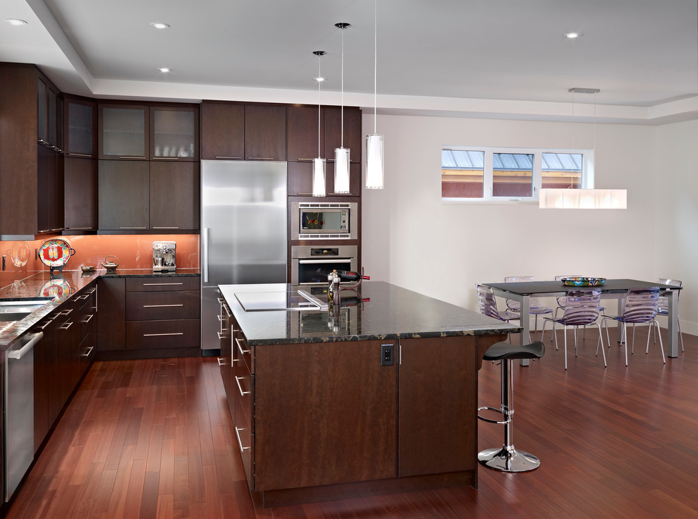 Design ideas for a contemporary l-shaped eat-in kitchen in Edmonton with flat-panel cabinets, dark wood cabinets, orange splashback, glass sheet splashback and stainless steel appliances.