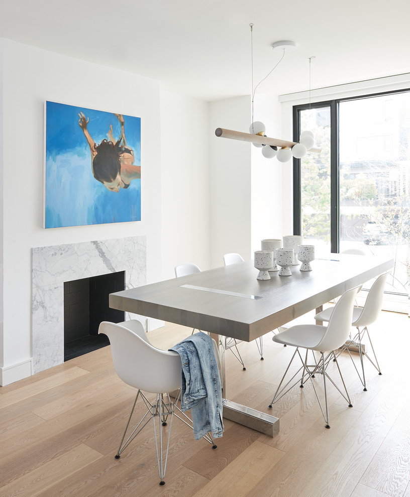 This is an example of a contemporary dining room in Toronto with white walls, light hardwood floors, a standard fireplace and beige floor.