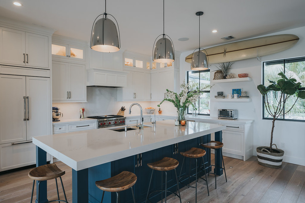 This is an example of a mid-sized beach style open plan kitchen in Other with a single-bowl sink, louvered cabinets, white cabinets, onyx benchtops, yellow splashback, stone slab splashback, stainless steel appliances, light hardwood floors, with island and brown floor.