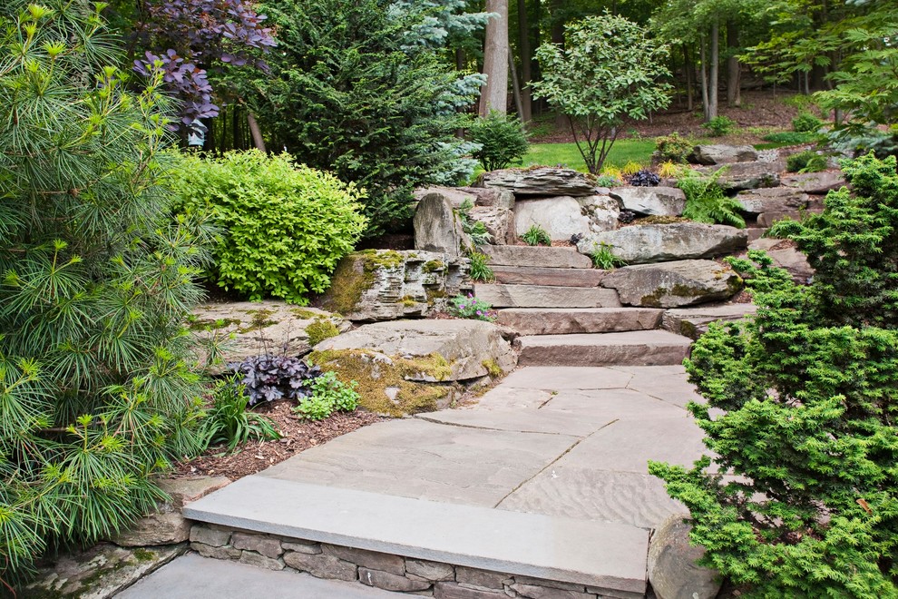 This is an example of a traditional sloped garden in New York with natural stone pavers and with rock feature.