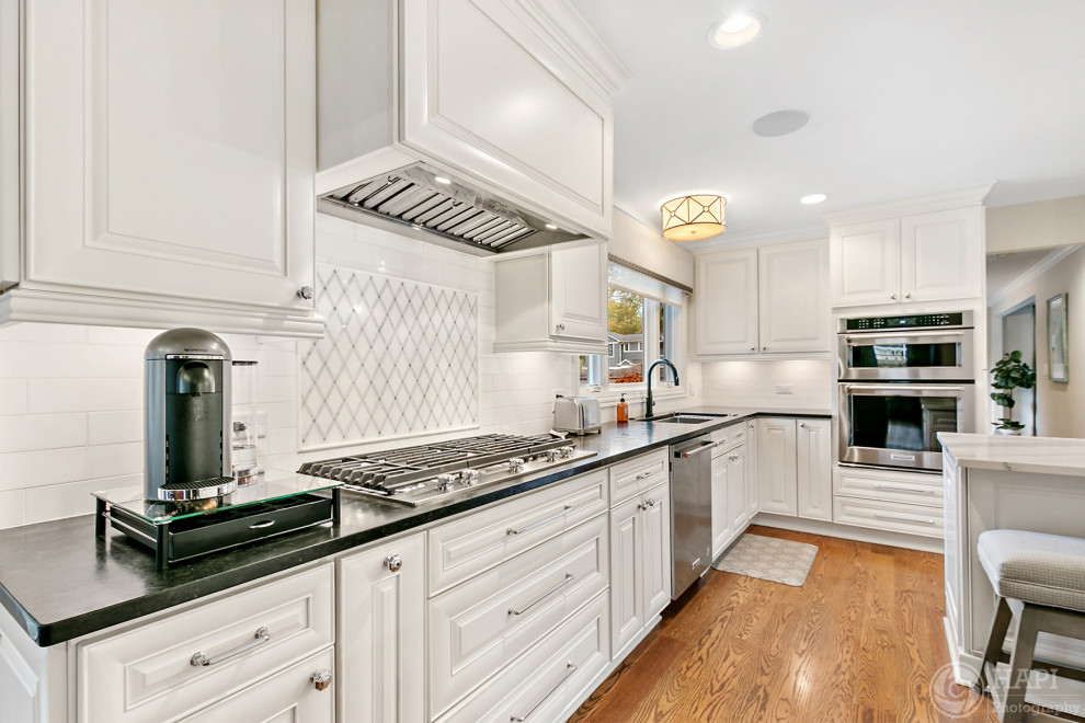 Example of a large transitional l-shaped kitchen design in Chicago with white cabinets, white backsplash, an island and black countertops