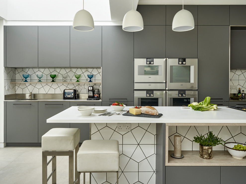 Inspiration for a contemporary single-wall open plan kitchen in London with an integrated sink, flat-panel cabinets, grey cabinets, solid surface benchtops, white splashback, ceramic splashback, stainless steel appliances, ceramic floors, with island and grey floor.