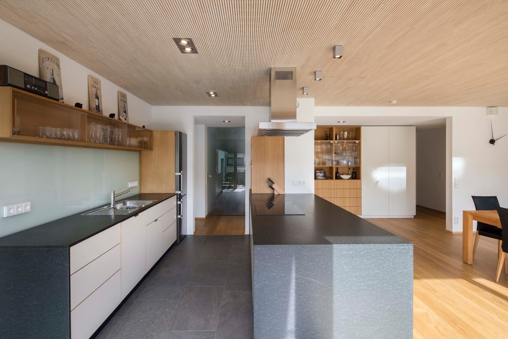 Küche mit weißen Schränken, Kücheninsel, schwarzem Boden, Einbauwaschbecken, flächenbündigen Schrankfronten, Küchenrückwand in Blau, Glasrückwand und Zementfliesen für Boden in Munich