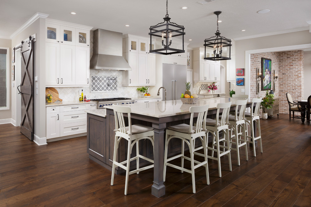 Design ideas for a transitional galley open plan kitchen in Houston with shaker cabinets, white cabinets, beige splashback, stainless steel appliances, dark hardwood floors, with island and beige benchtop.