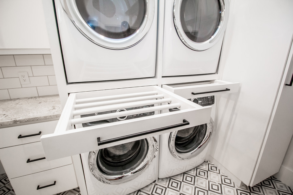 Design ideas for a mid-sized contemporary l-shaped utility room in Other with an undermount sink, flat-panel cabinets, white cabinets, granite benchtops, white walls, a stacked washer and dryer and multi-coloured floor.
