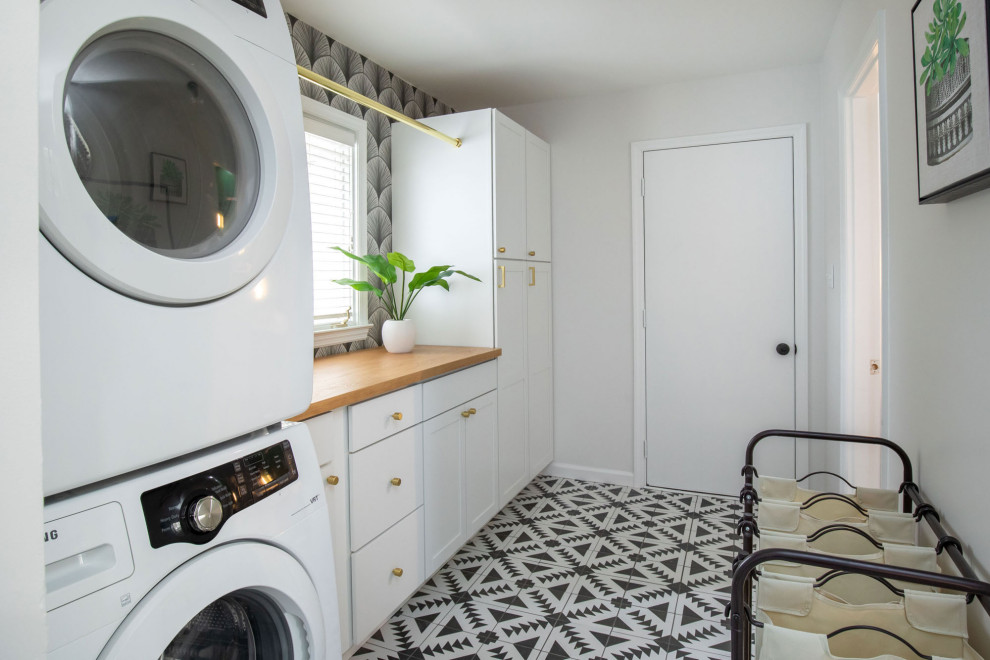Photo of a mid-sized transitional galley dedicated laundry room in Indianapolis with shaker cabinets, white cabinets, wood benchtops, white walls, ceramic floors, a stacked washer and dryer, black floor and beige benchtop.
