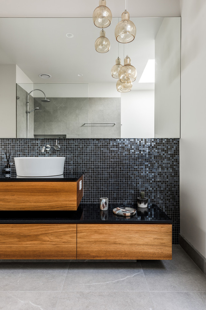 Photo of a contemporary bathroom in Melbourne with medium wood cabinets, a freestanding tub, an open shower, a one-piece toilet, gray tile, porcelain tile, white walls, porcelain floors, a vessel sink and engineered quartz benchtops.