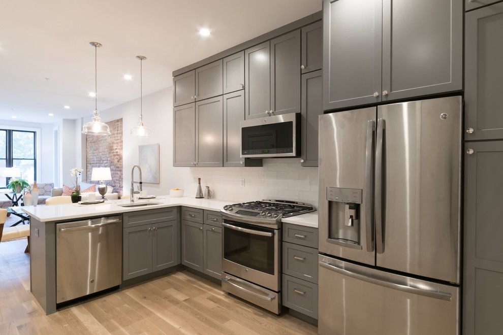 Open concept kitchen - small transitional l-shaped medium tone wood floor and brown floor open concept kitchen idea in DC Metro with a single-bowl sink, shaker cabinets, gray cabinets, quartz countertops, white backsplash, ceramic backsplash, stainless steel appliances and a peninsula