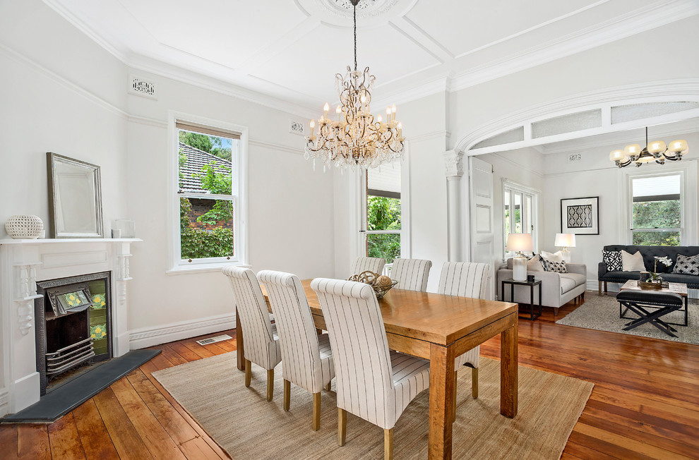 This is an example of a large transitional dining room in Sydney with medium hardwood floors, a corner fireplace, a plaster fireplace surround, brown floor and white walls.