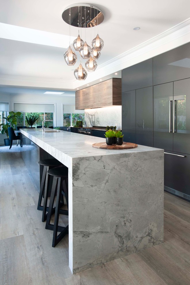 Large contemporary galley open plan kitchen in Sydney with a drop-in sink, marble benchtops, stone slab splashback, black appliances and with island.