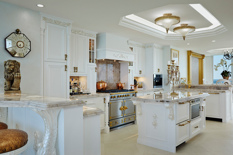 Traditional u-shaped open plan kitchen in Miami with recessed-panel cabinets, white cabinets, beige splashback, stone slab splashback, with island, beige floor and beige benchtop.