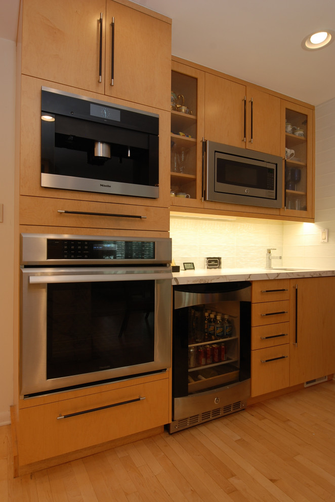 This is an example of a mid-sized contemporary u-shaped eat-in kitchen in Chicago with an undermount sink, flat-panel cabinets, light wood cabinets, quartzite benchtops, white splashback, subway tile splashback, stainless steel appliances, light hardwood floors, yellow floor and white benchtop.