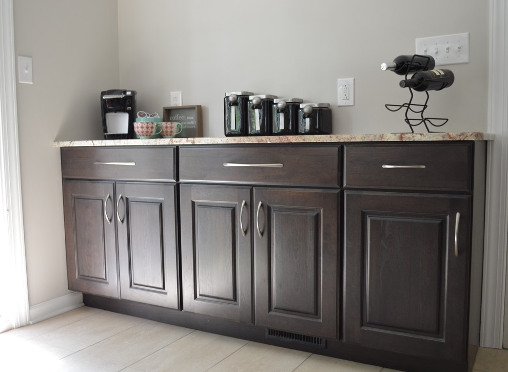 Large transitional l-shaped porcelain tile and beige floor eat-in kitchen photo with a farmhouse sink, raised-panel cabinets, brown cabinets, granite countertops, white backsplash, ceramic backsplash, stainless steel appliances and a peninsula