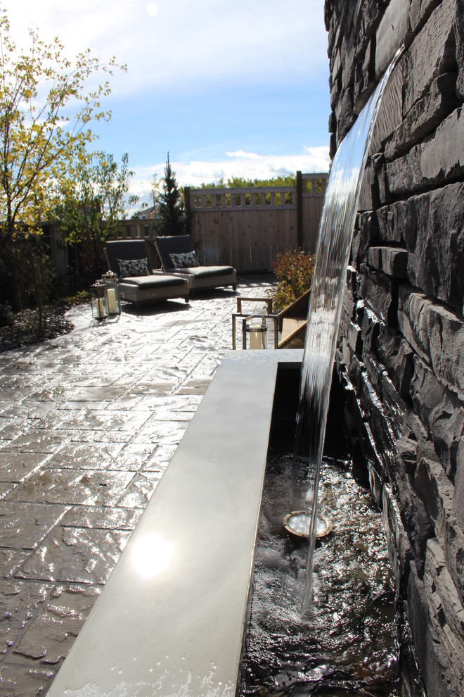 Photo of a small contemporary backyard patio in Calgary with a water feature, concrete pavers and no cover.
