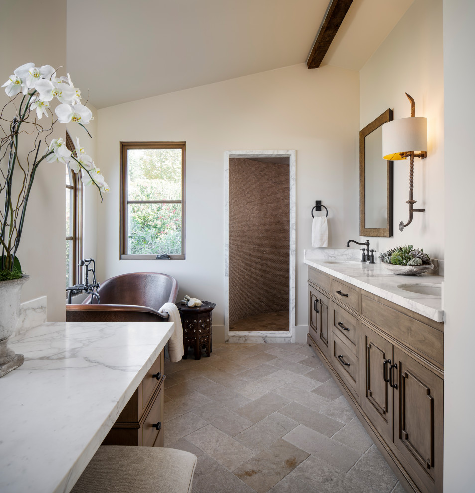 Example of a tuscan beige floor, double-sink and vaulted ceiling freestanding bathtub design in Los Angeles with recessed-panel cabinets, medium tone wood cabinets, beige walls, an undermount sink, white countertops and a built-in vanity