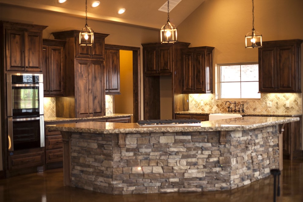 Large country l-shaped eat-in kitchen in Oklahoma City with a farmhouse sink, raised-panel cabinets, dark wood cabinets, granite benchtops, stone tile splashback, stainless steel appliances, concrete floors, with island and multi-coloured splashback.