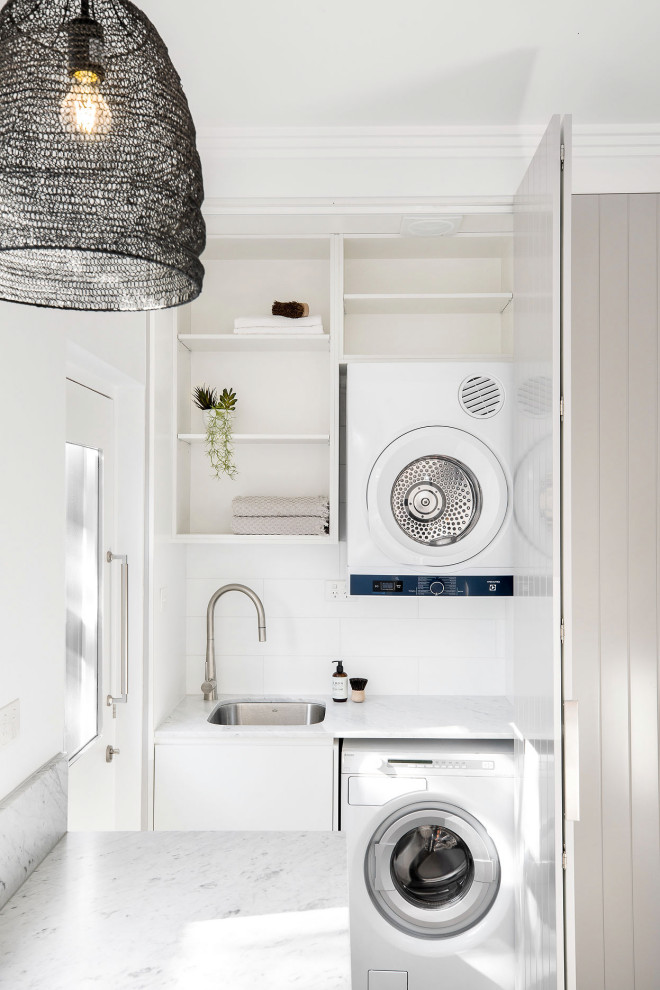 Inspiration for a small single-wall dedicated laundry room in Sydney with a drop-in sink, shaker cabinets, beige cabinets, marble benchtops, white splashback, marble splashback, white walls, light hardwood floors, a stacked washer and dryer, beige floor and white benchtop.