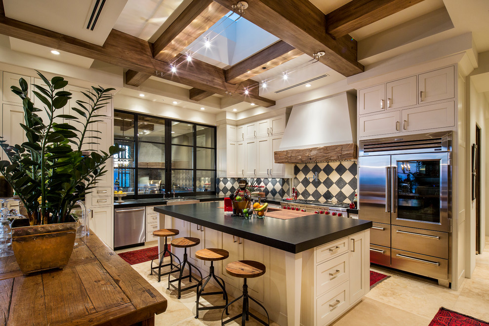 Photo of a l-shaped kitchen in Phoenix with shaker cabinets, beige cabinets, multi-coloured splashback, stainless steel appliances, with island, beige floor and black benchtop.