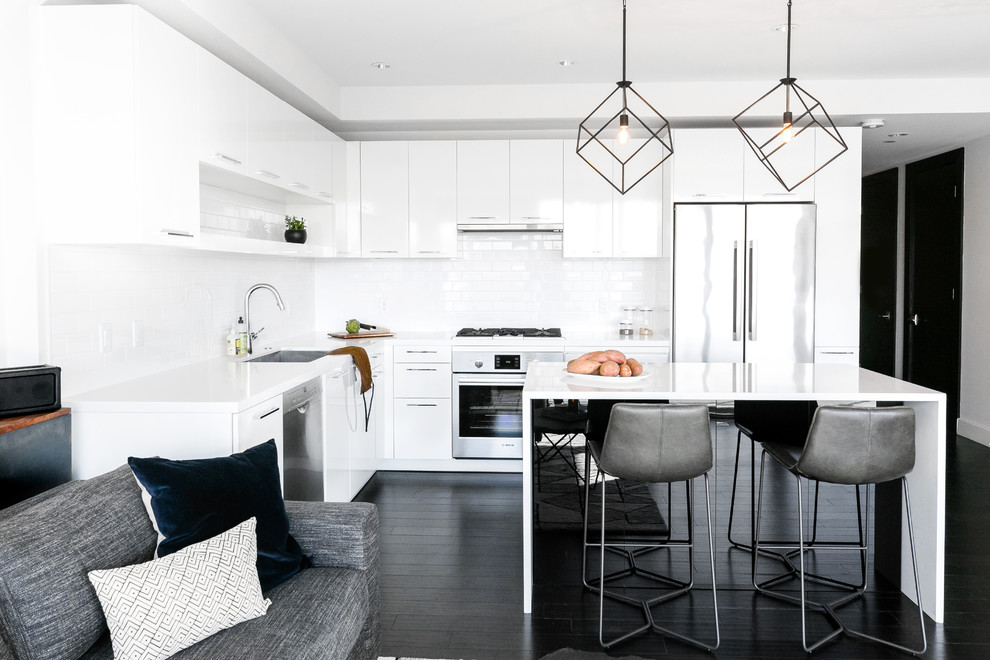 Large contemporary l-shaped eat-in kitchen in Phoenix with an undermount sink, flat-panel cabinets, white cabinets, quartz benchtops, white splashback, subway tile splashback, stainless steel appliances, dark hardwood floors, with island, white benchtop and black floor.