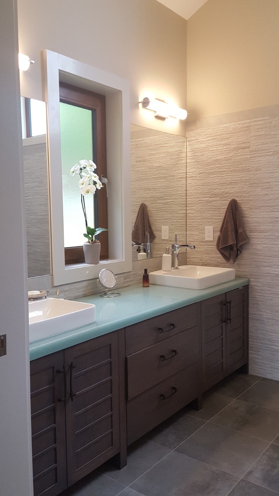 Photo of a mid-sized contemporary master bathroom in New York with flat-panel cabinets, dark wood cabinets, beige tile, stone tile, beige walls, porcelain floors, a vessel sink and glass benchtops.
