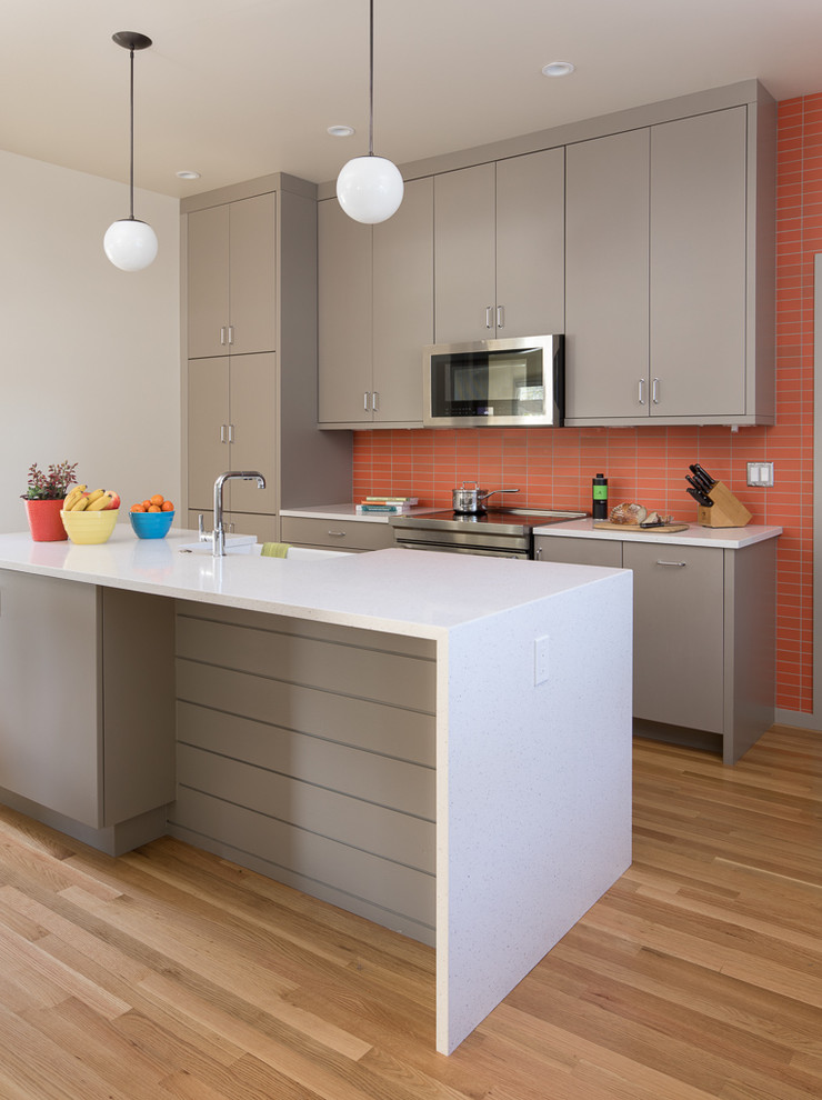 Inspiration for a midcentury galley kitchen in Portland with a farmhouse sink, flat-panel cabinets, grey cabinets, orange splashback, stainless steel appliances, light hardwood floors, a peninsula, beige floor and white benchtop.