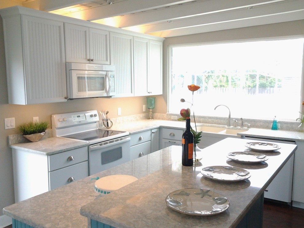 This is an example of a mid-sized beach style kitchen in Tampa with a farmhouse sink, louvered cabinets, white cabinets, granite benchtops, white appliances, dark hardwood floors, with island and brown floor.