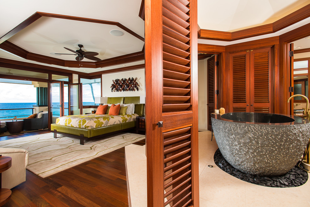 This is an example of a large tropical master bedroom in Hawaii with beige walls and dark hardwood floors.