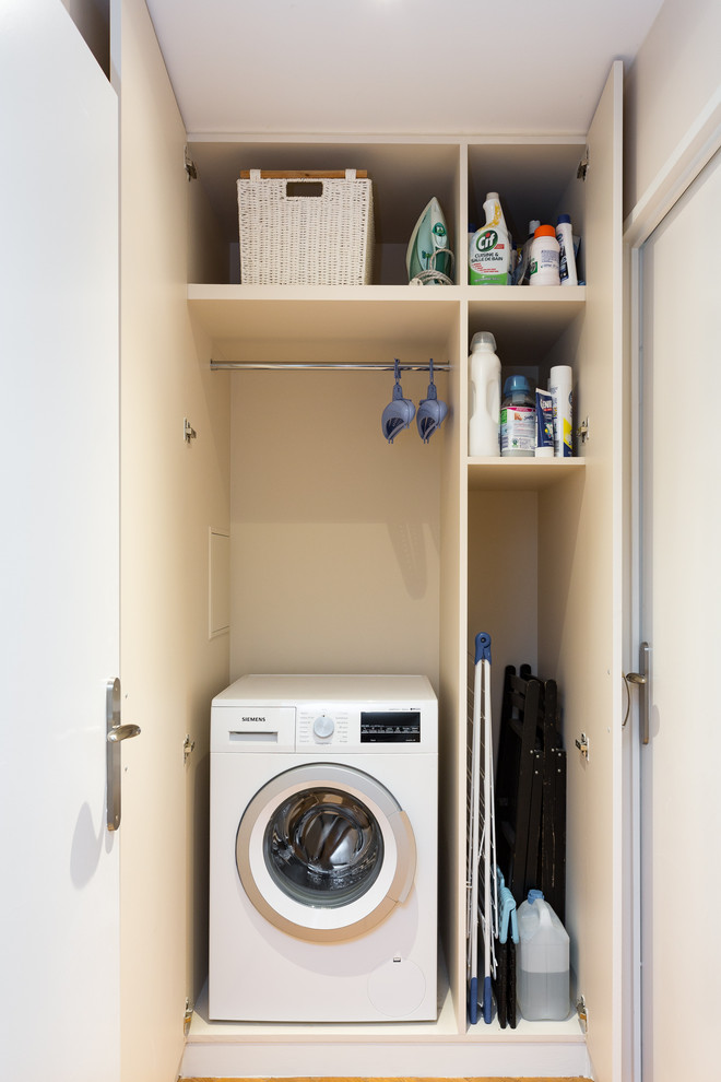 Design ideas for a small modern single-wall laundry cupboard in Other with flat-panel cabinets, white cabinets, white walls, light hardwood floors, an integrated washer and dryer and beige floor.