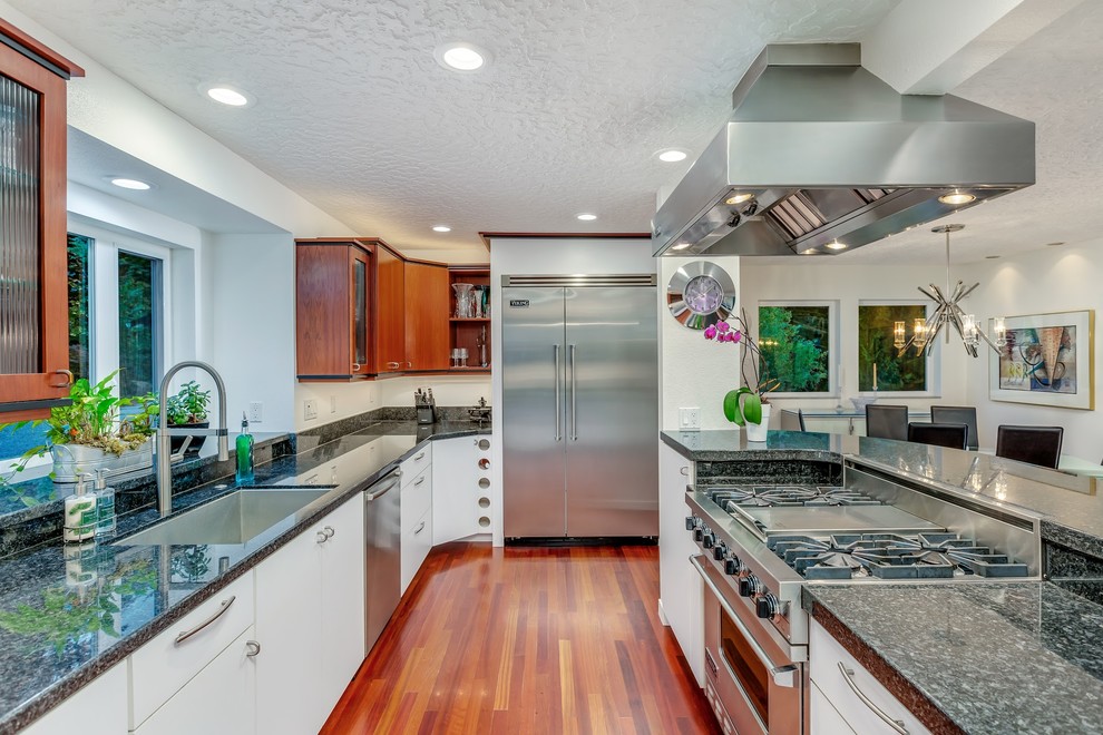 This is an example of a mid-sized modern galley eat-in kitchen in Portland with a single-bowl sink, flat-panel cabinets, dark wood cabinets, granite benchtops, white splashback, stone slab splashback, stainless steel appliances, dark hardwood floors, multi-coloured floor and black benchtop.
