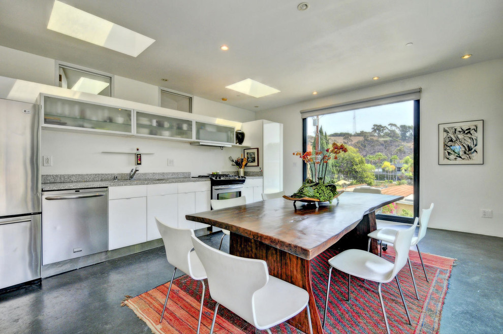 This is an example of a mid-sized contemporary single-wall eat-in kitchen in Los Angeles with a drop-in sink, flat-panel cabinets, white cabinets, granite benchtops, stainless steel appliances, concrete floors, grey splashback, stone slab splashback, no island and grey floor.