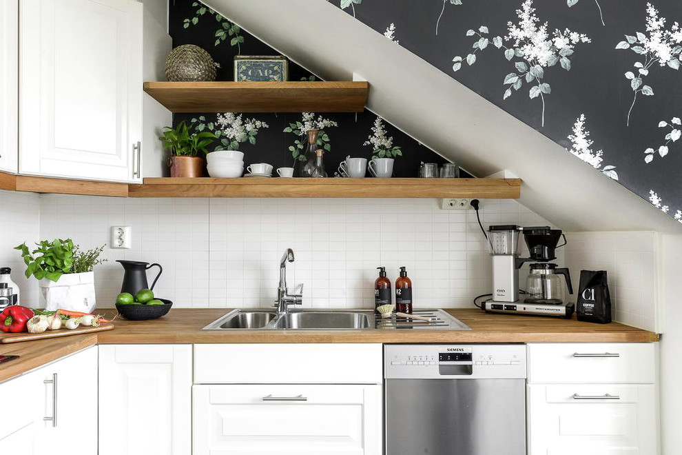 Photo of a scandinavian l-shaped kitchen in Other with a double-bowl sink, raised-panel cabinets, white cabinets, wood benchtops, white splashback, subway tile splashback and stainless steel appliances.
