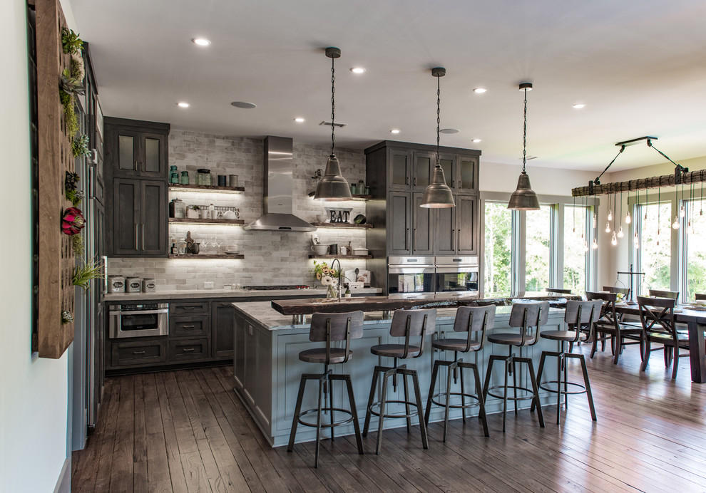 Photo of a large country l-shaped eat-in kitchen in Charleston with shaker cabinets, stainless steel appliances, with island, brown floor, dark wood cabinets, a farmhouse sink, quartzite benchtops, grey splashback, stone tile splashback and dark hardwood floors.