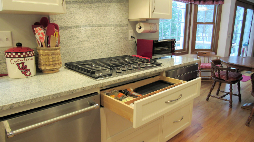 Example of a mid-sized transitional l-shaped light wood floor and brown floor eat-in kitchen design in Boston with an undermount sink, recessed-panel cabinets, white cabinets, granite countertops, gray backsplash, granite backsplash, stainless steel appliances, an island and gray countertops