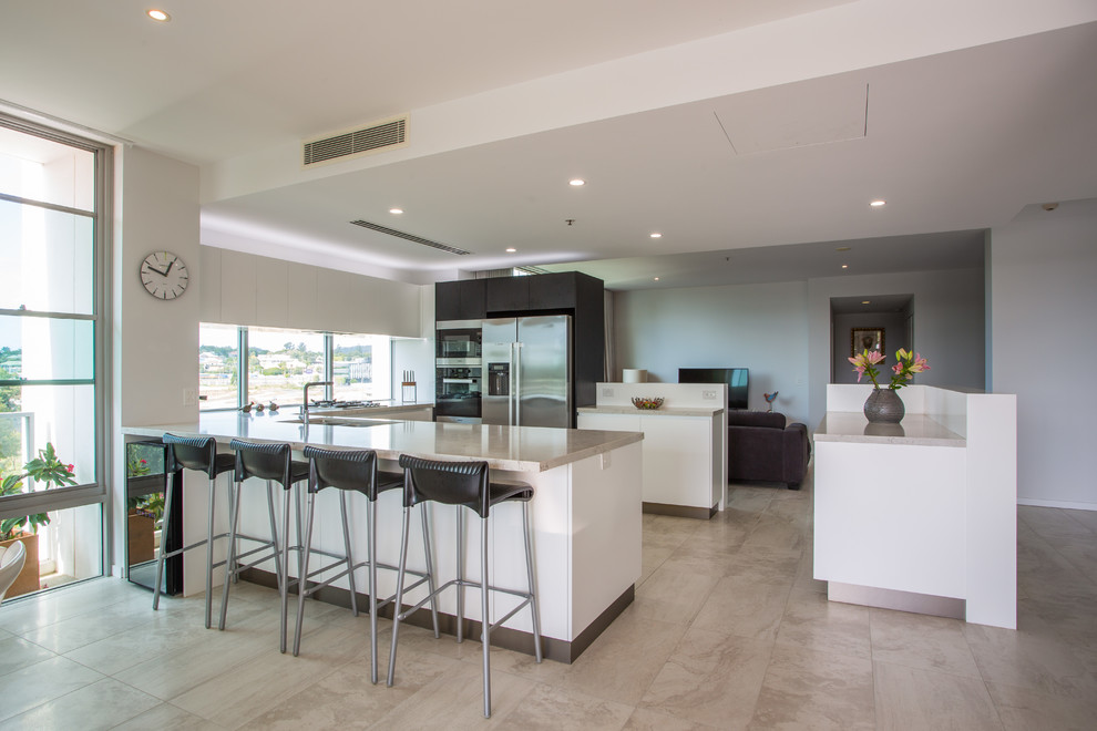 This is an example of a large modern u-shaped open plan kitchen in Brisbane with a double-bowl sink, stainless steel appliances, brown benchtop, recessed-panel cabinets, white cabinets, solid surface benchtops, porcelain floors, multiple islands and brown floor.