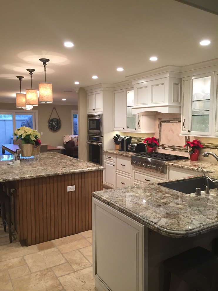 Large traditional l-shaped eat-in kitchen in Orange County with raised-panel cabinets, granite benchtops, beige splashback, stainless steel appliances, travertine floors, with island, a single-bowl sink, white cabinets, travertine splashback, brown floor and multi-coloured benchtop.
