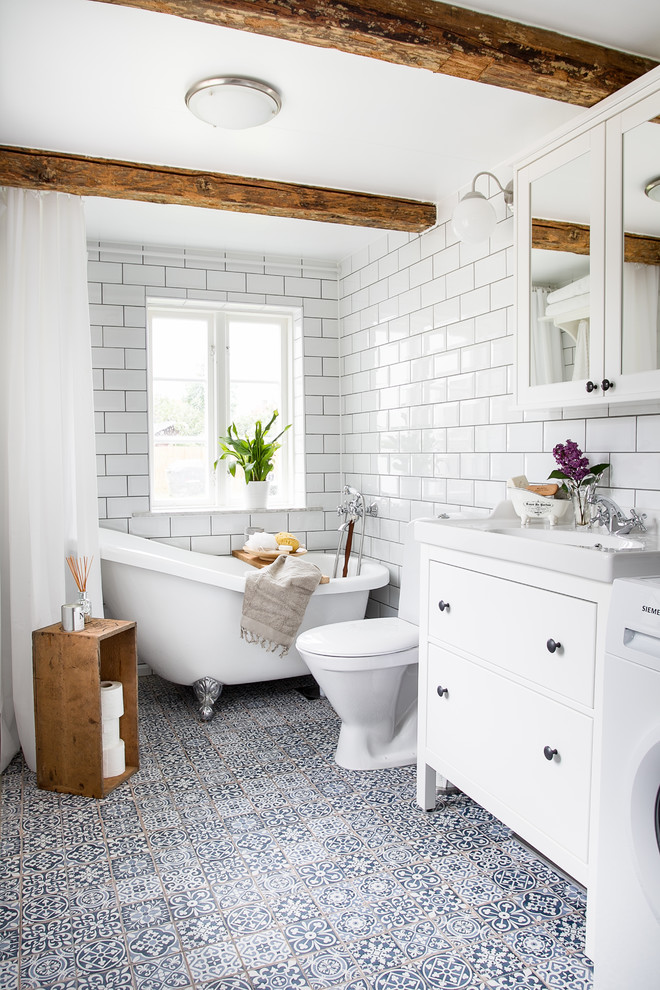 Mid-sized country 3/4 bathroom in Malmo with white cabinets, a claw-foot tub, a shower/bathtub combo, a one-piece toilet, white tile, white walls, cement tiles, subway tile, a console sink, blue floor, a shower curtain and flat-panel cabinets.