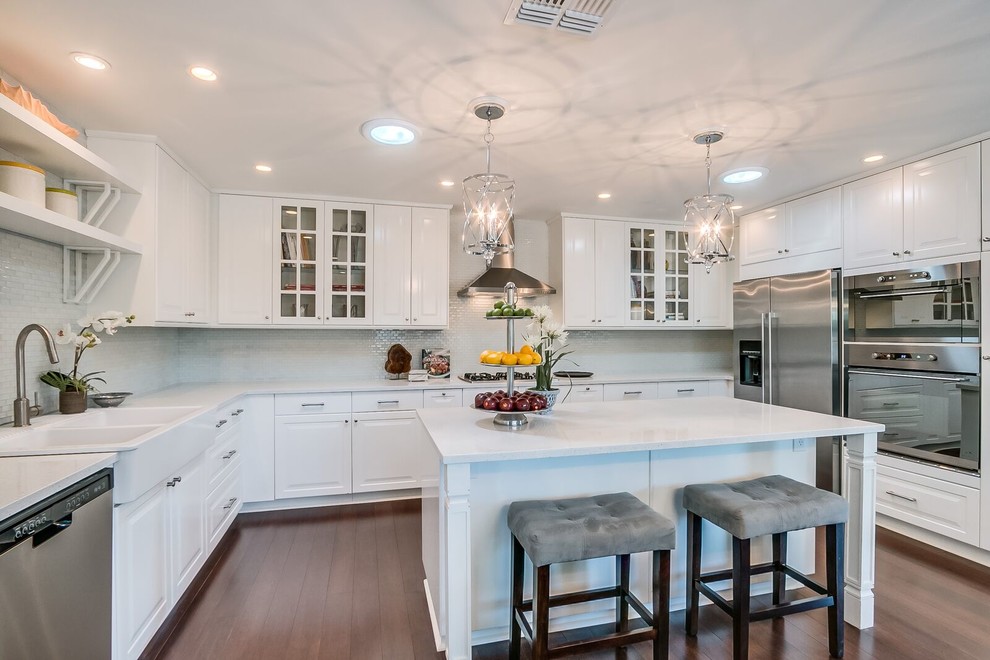 Mid-sized transitional u-shaped medium tone wood floor and brown floor open concept kitchen photo in Phoenix with raised-panel cabinets, white cabinets, quartz countertops, white backsplash, matchstick tile backsplash, stainless steel appliances and an island