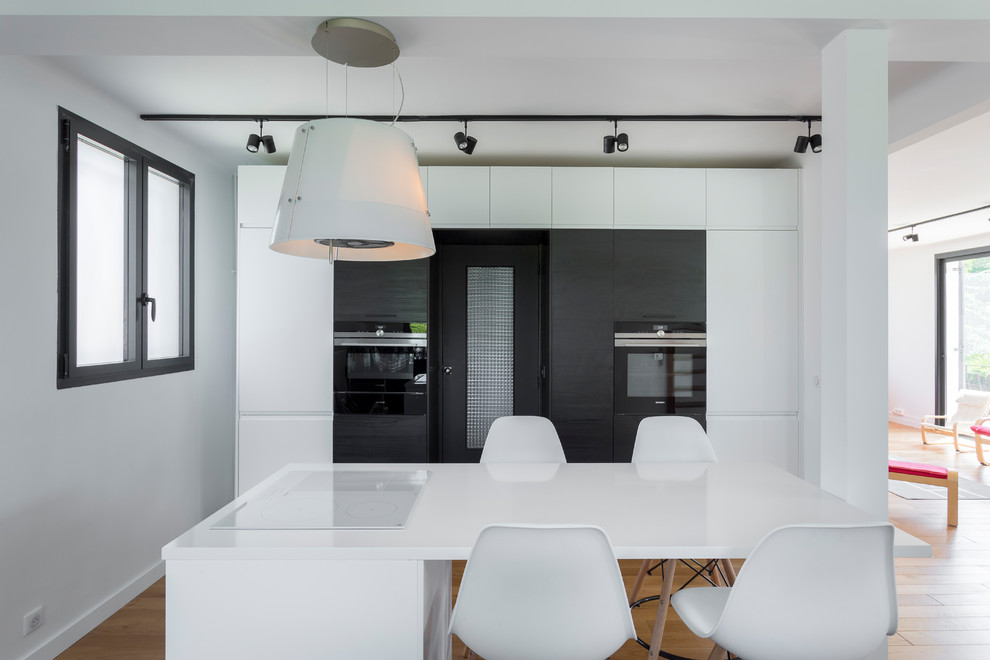 This is an example of a large contemporary galley open plan kitchen in Other with an undermount sink, beaded inset cabinets, black cabinets, quartzite benchtops, blue splashback, ceramic splashback, black appliances, light hardwood floors, with island, beige floor and white benchtop.
