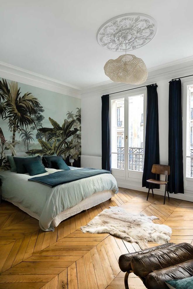 Large scandinavian master bedroom in Paris with white walls, light hardwood floors, no fireplace and brown floor.