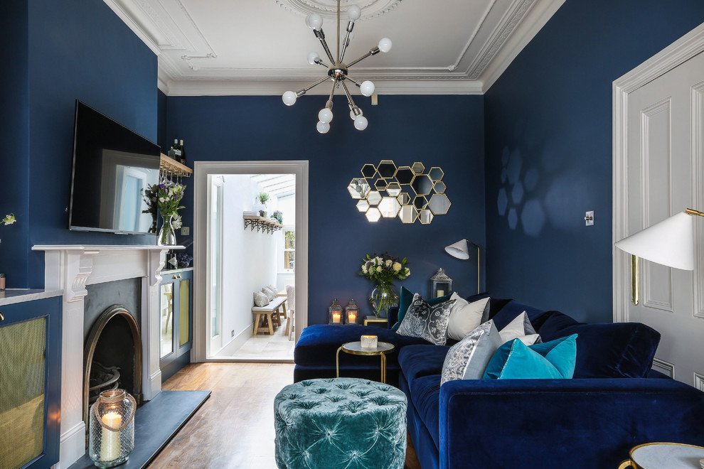 This is an example of a small transitional enclosed living room in London with a home bar, blue walls, medium hardwood floors, a standard fireplace, a stone fireplace surround, a wall-mounted tv and brown floor.