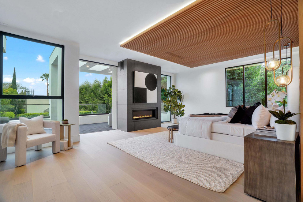 Inspiration for a large modern master bedroom with white walls, light hardwood flooring, a standard fireplace, a tiled fireplace surround, brown floors, a wood ceiling and wood walls.