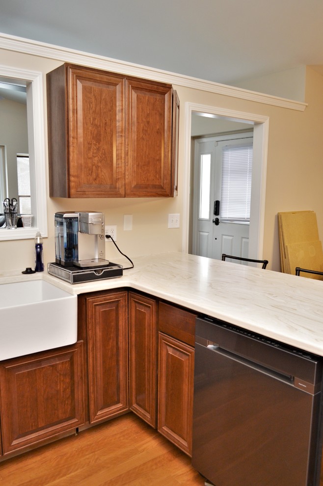 Mid-sized traditional u-shaped eat-in kitchen in Chicago with a farmhouse sink, raised-panel cabinets, brown cabinets, solid surface benchtops, a peninsula and white benchtop.
