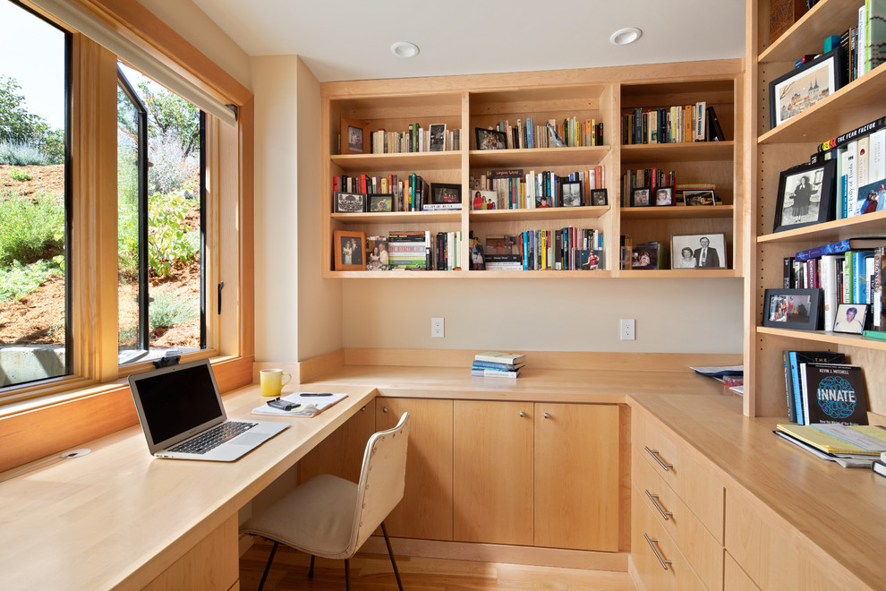 Photo of a contemporary home office in San Francisco with a library, beige walls, light hardwood floors, no fireplace, a built-in desk and beige floor.