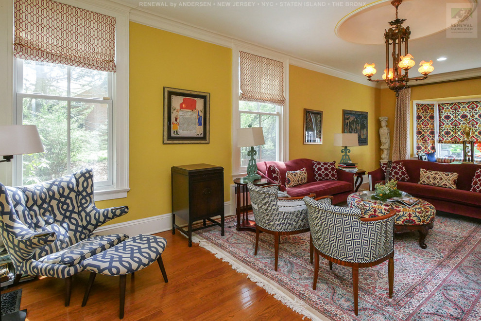 Cette image montre un grand salon fermé avec une salle de réception, un mur jaune, un sol en bois brun, une cheminée standard, un manteau de cheminée en brique, un téléviseur fixé au mur et un sol multicolore.