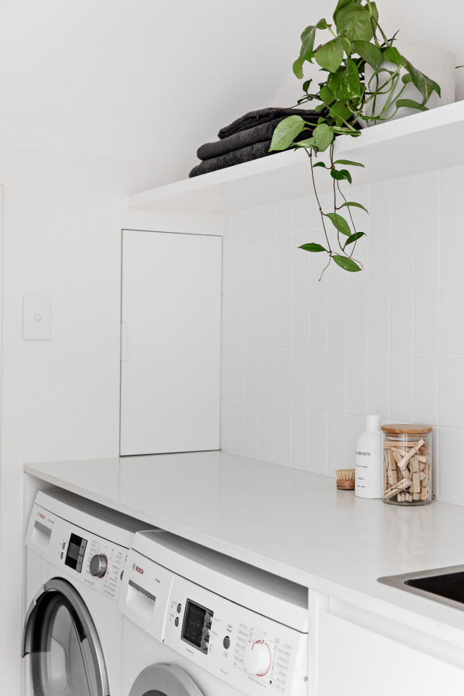 Photo of a small contemporary single-wall dedicated laundry room in Sydney with a drop-in sink, open cabinets, white cabinets, quartz benchtops, white splashback, ceramic splashback, white walls, porcelain floors, a side-by-side washer and dryer, grey floor and white benchtop.