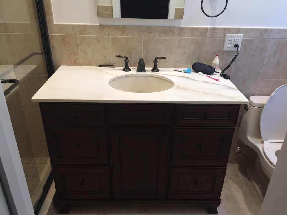 Photo of a 3/4 bathroom in New York with raised-panel cabinets, dark wood cabinets, a corner shower, beige tile, ceramic tile, ceramic floors, an undermount sink, marble benchtops, beige floor and a sliding shower screen.