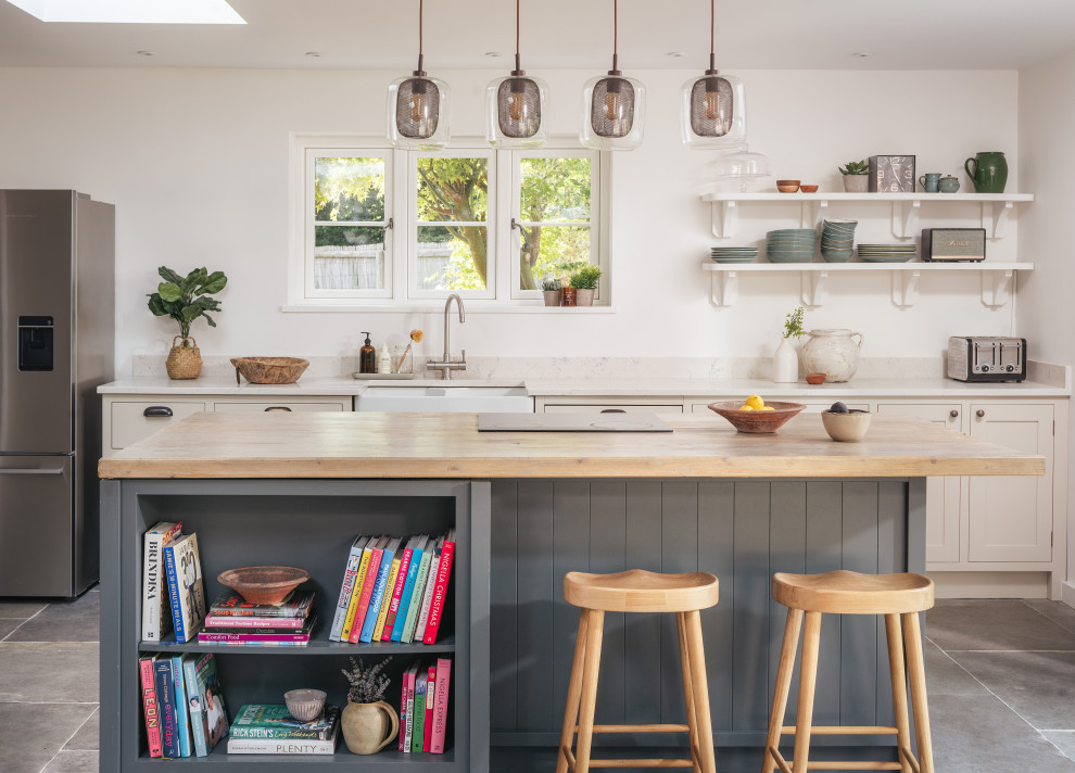 Medium sized rural open plan kitchen in Gloucestershire with a belfast sink, recessed-panel cabinets, beige cabinets, quartz worktops, slate flooring, grey floors, beige worktops and an island.