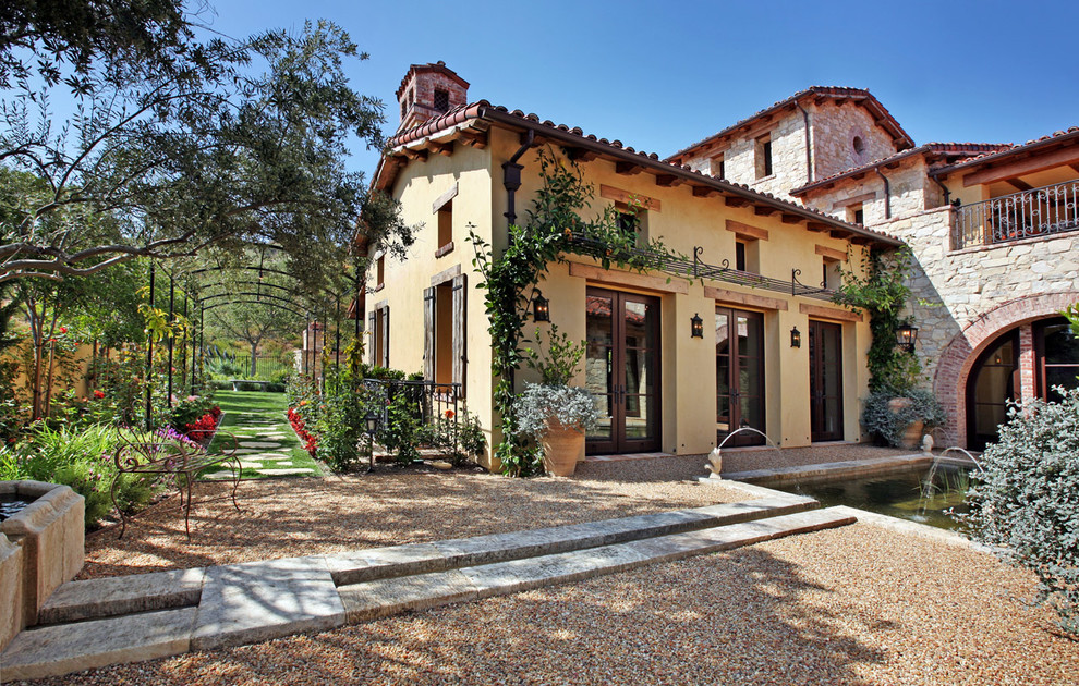 Mid-sized mediterranean two-storey grey house exterior in Orange County with a gable roof, stone veneer and a tile roof.